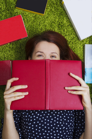 Woman's portrait smiling feeling happy with books lying on green artificial grass.の写真素材