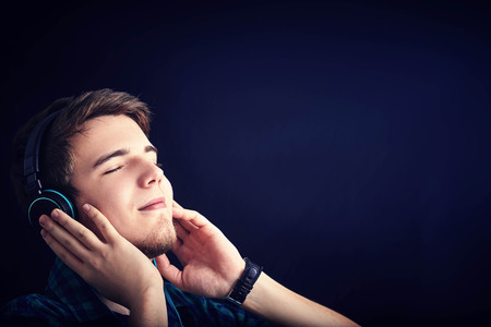 Young man student listening to music with pleasure isolated on black background.の写真素材