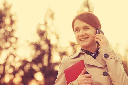 Young smiling businesswoman, student professional outdoors talking on cell smart phone and holding a red journal.Businesswoman smiling, Life style,の写真素材