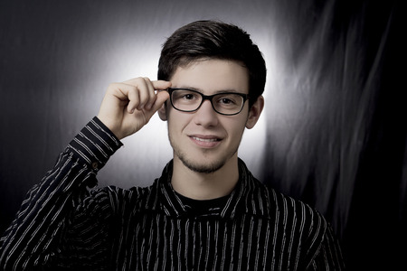 Smiling Student portrait of a young men wearing black glasses and holding them isolated on black background.Facial expressionの写真素材