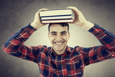 Smiling student young man holding books on his head over grey background.の写真素材