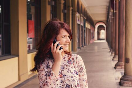 Smiling young girl talking on mobile phone in a city .Young smiling student girl outdoors talking on...