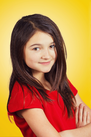 Portrait of a beautiful and confident little girl looking to camera isolated on yellow background.の写真素材