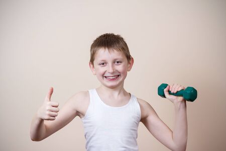 Smiling Happy little boy holding thumb up looking at camera while exercising with dumbbell.Healthy life, strong little boy, sport.の写真素材