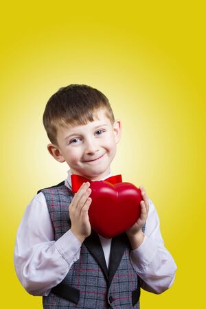 Happy, smiling little boy holding Red heart isolated on yellow background.Concept Love, Care, Health.Facial expression.の写真素材