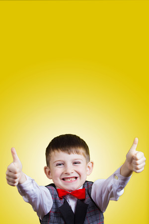 Smiling Happy Joyful beautiful little boy with thumb up looking at camera.Closeup Studio Portrait isolated on yellow background.の写真素材