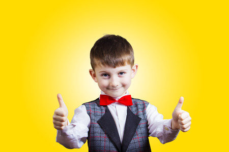 Portrait of happy little boy showing thumbs up gesture wearing costume and a red bow isolated over yellow background.Funnyhappiness.の写真素材
