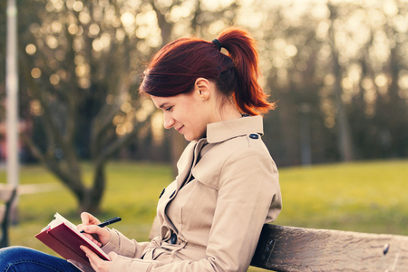 Young smiling businesswoman sitting in a classic city park, student professional outdoors holding a red, journal writing in it.Businesswoman smiling, Life style,の写真素材