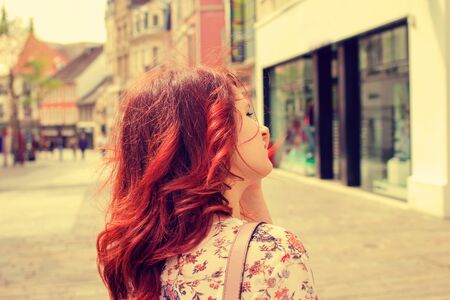 Red head Young woman on a shopping day portrait in a city.Young woman walking with raised hand in her hair .Life styleの写真素材