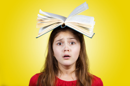 Bored Tired cute little schoolgirl  with a open book on her head  isolated over yellow background.の写真素材
