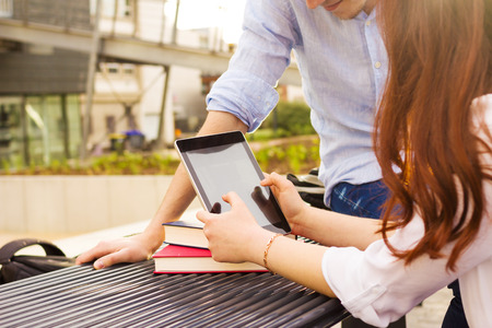 Young student woman taping on tablet in a city on university bench .Young student  outdoors with tablet.Life style.Cityの写真素材