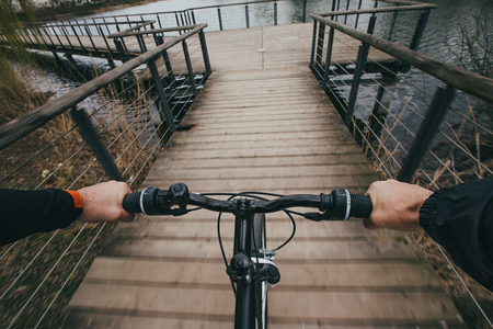 Close-up image of cyclist man hands on handlebar riding bike in park, face is not visible.Young man...