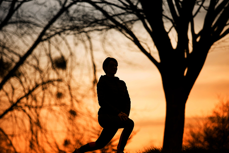 Young Woman stretching neer tree in a sunrise.Female fitness outside doing stretch exercises in morning before a run.の写真素材