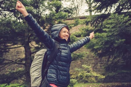 Smiling Student woman with raised hands hiking in forest. Female hiker smiling happy portrait on rainy day during a trekking trip. Pretty young girl outdoors in nature.の写真素材