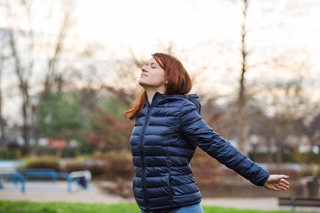 Young woman breathing fresh air before a run.Freedom happy young woman feeling alive and free in a city park in nature with arms raised up.の写真素材