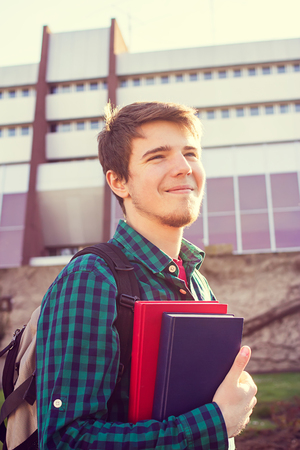 University.Smiling young student man holding a book and a bag on a university background .Young smiling student  outdoors Life style.City.Student.の写真素材