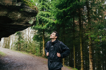 Young Man,Student hiking in forest.Man hiker smiling happy portrait looking up enjoying nature on foggy day during a trekking trip. Back of a young man outdoors in nature on a hiker path in forest.の写真素材