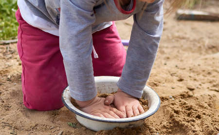 Closeup of a child hands, playing in the sand with metal dish in village areaの写真素材