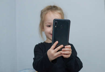 Surprised happy smilling little child girl using mobile phone