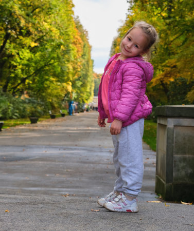 pretty happy beautiful smiling little girl pink clothes posing park alley autumnの写真素材