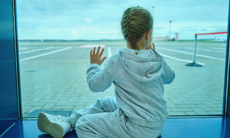 Little girl kid children looking waiting through window to airplane in airportの写真素材
