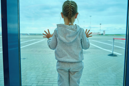 Little girl children looking waiting through window to airplane in airport