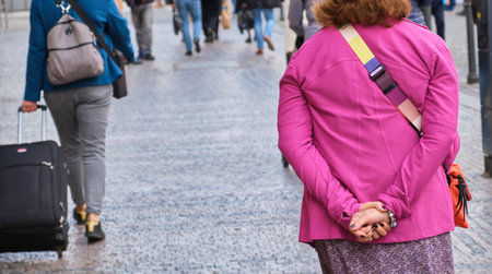 Elderly woman pink jacket outdoors hands on back while walking city pathwayの写真素材