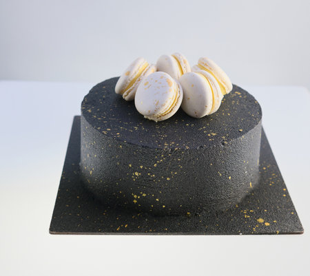 Black birthday cake decorated with gold macarons white backgroundの写真素材