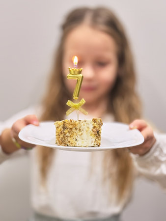 Blurred portrait Cute happy little seven years old Girl holding slice of birthday cake with number 7 at a party celebrationの写真素材