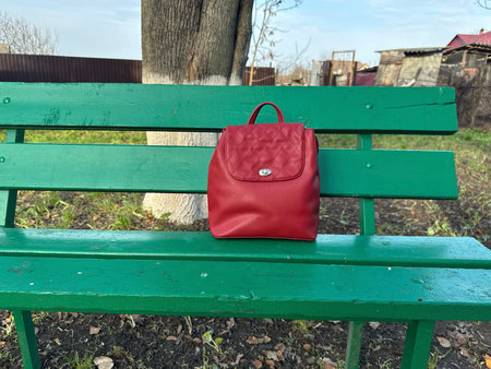 A red backpack rests on a green park bench, exuding tranquility. Perfect for travel, fashion, or lifestyle themes. Evokes peacefulness, simplicity, and readiness for journeyの写真素材