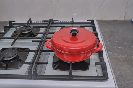 A vibrant red pot sits on a gas stove, promising a delicious meal. Perfect for illustrating home cooking, healthy eating, and cozy kitchen scenes. Use for recipes & lifestyleの写真素材