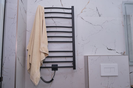 A modern bathroom featuring a heated towel rack with a beige towel, creating a comfortable and stylish atmosphere. Ideal for home decor, interior design promotion. Clean designの写真素材