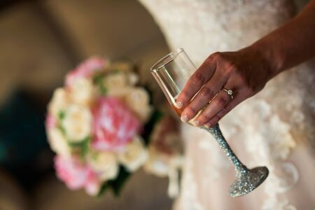 Bride wearing ring holding champagne glass and bouquetの写真素材