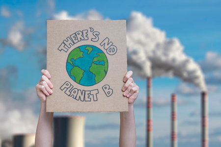 Hands holding cardboard with environmental poster against nuclear power plant in the sky