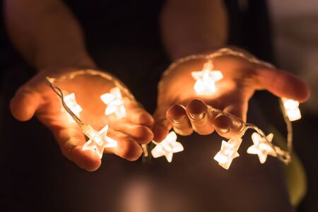 Hands holding shiny Christmas lights with star shapesの写真素材
