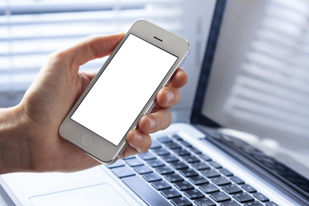 Smartphone with blank screen in the hand of business woman working in office with laptopの写真素材