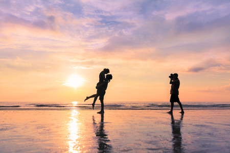 Photographer taking photo of a couple kissing on the beach during sunset - concept about romantic...