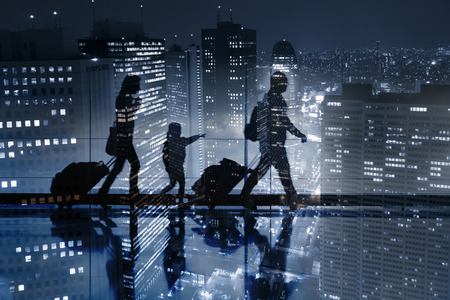 Double exposure of passengers walking with luggage and a beautiful aerial view of a large city with skyscrapers at night in backgroundの写真素材