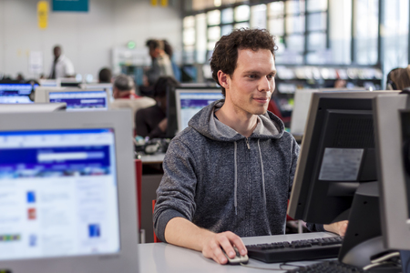 Smiling student using a computer in a library to perform some researches for high school