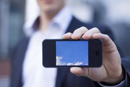 Businessman showing smartphone screen with office buildings in backgroundの写真素材