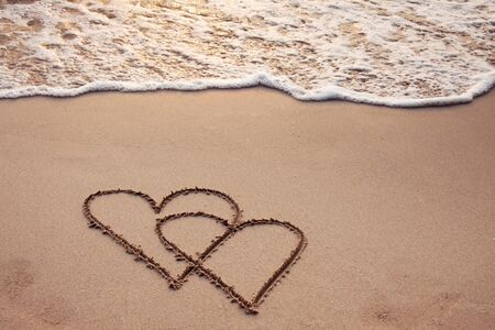 Hearts drawn in the sand with seafoam and waveの写真素材