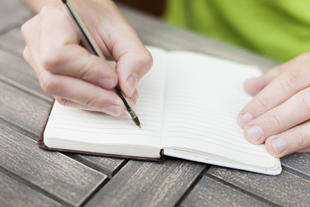Young man writing notes on a notebook with a pen, close-up view of handsの写真素材