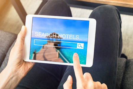 Person searching hotel room to book online with a tablet computer and using a search engine website, planning vacationsの写真素材