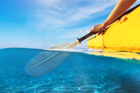 Split view of person kayaking in transparent blue sea, underwater and above water photography of kayak and paddle in warm summer tropical travel destination for vacation holidaysの写真素材
