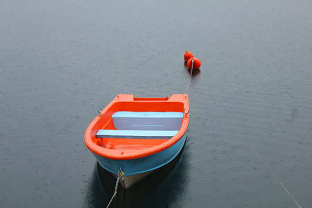a blu and orange boat on the lake under the rainの写真素材