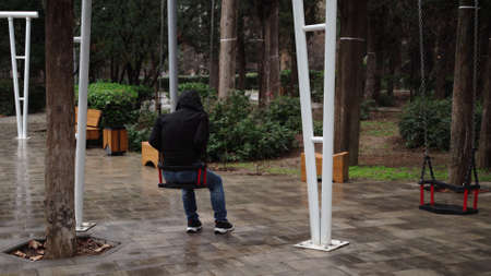 Lonely man in the park swinging on a swing. A sad man in depression is lonely swinging on a swing in...