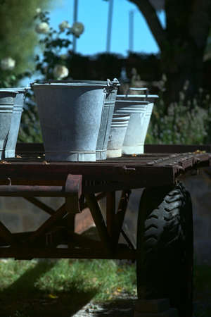 Tin buckets on a cart in a yard at noon in summerの写真素材