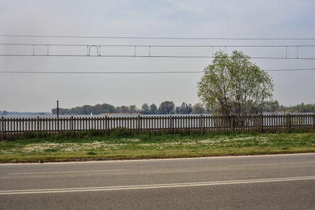 Road next to a lake and a park with railroad tracks by its edge on a sunny dayの写真素材