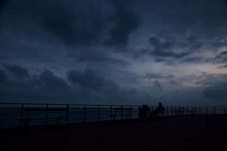 People sitting next to a rail by the seaside at duskの写真素材