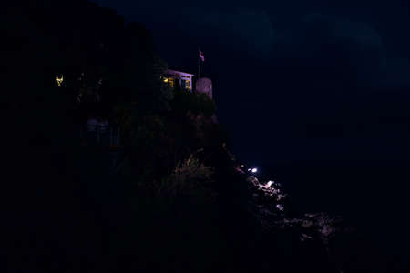 Building on the top of a cliff lit by a purple light at nightの写真素材